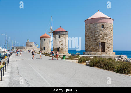 Rhodos, Griechenland - 20. August 2015: Passanten in einem Hafen in der Nähe von Windmühlen und Fort von St. Nikolaus in der Stadt Rhodos, Griechenland Stockfoto