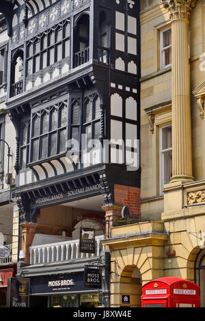 England, Cheshire, Chester, Iconic rote Telefonzelle in ATM am Eastgate Street mit schwarzen und weißen Architektur hinter konvertiert. Stockfoto