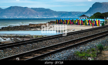 Bunte Strandhütten am Meer, Muizenbery Beach, False Bay, Western Cape, Südafrika, neben Bahngleisen und Blick auf ferne Berge in der Nähe von Hout Bay Stockfoto