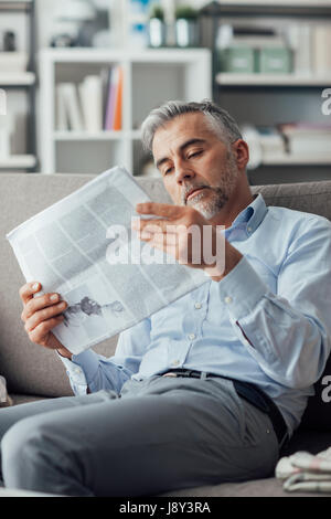 Zuversichtlich Geschäftsmann Lesen einer Zeitung zu Hause, er ist auf der Couch sitzen und entspannen Stockfoto