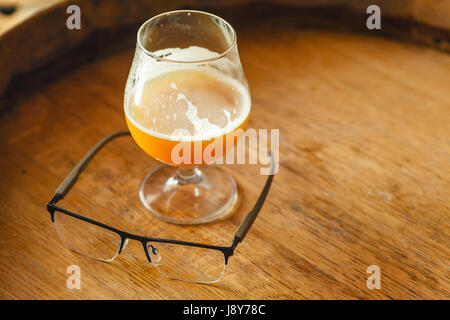 Wehat Bier mit einer Brille stehend auf einem Holzfass in einer Brauerei Stockfoto