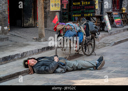 Mann schläft auf der Straße neben seinem Fahrrad, Pingyao, Shanxi Provinz, China Stockfoto