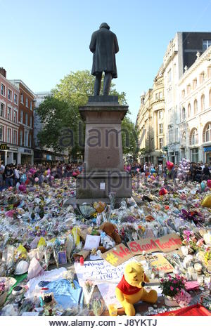 Menschen stehen und Hommage an die Opfer der Manchester Bombardierung in St Ann's Square Manchester an einem Denkmal von Blumen und anderen Objekten Stockfoto