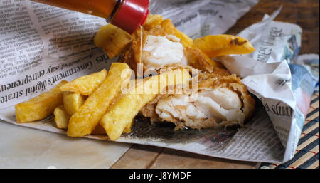 Hinzufügen von Essig auf eine englische Fish &amp; Chips in Zeitungspapier, die traditionelle Art eingewickelt Stockfoto