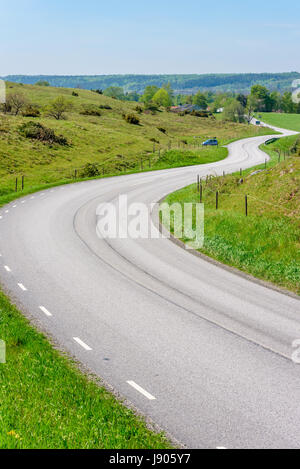 Kurvenreiche Straße durch malerische Landschaft. Hügeln und Wiesen entlang der kurvenreichen Straße. Lage Brosarp in Scania, Schweden. Kopieren Sie Raum unterwegs. Stockfoto