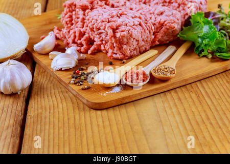 rohes Hackfleisch vom Schwein, mit Knoblauch, schwarzem Pfeffer und Zwiebeln auf einem Holztisch Stockfoto