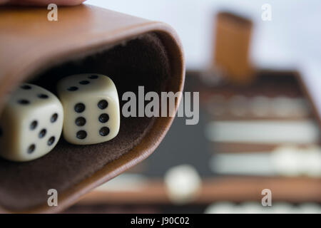 Bereitet, um Backgammon Würfel auf die braun und Creme Backgammon-Brett im Hintergrund unscharf. Fokussierung auf die Würfel in den Würfelbecher. Stockfoto