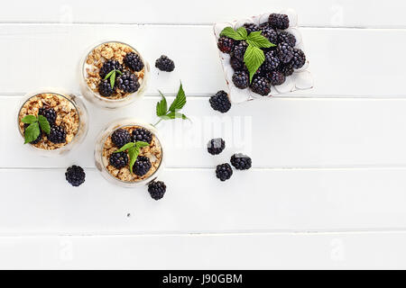 BlackBerry Parfaits mit griechischem Joghurt, Müsli und frischen Brombeeren gemacht Schuss von oben weißer Holztisch. Raum für Textfreiraum. Stockfoto