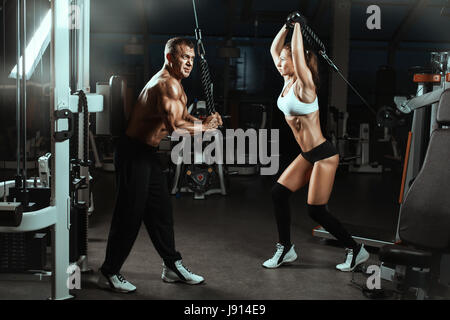 Mann und Frau trainiert Muskeln im Fitness-Studio.  Sie trainieren mit Maschinen für Bodybuilder. Stockfoto