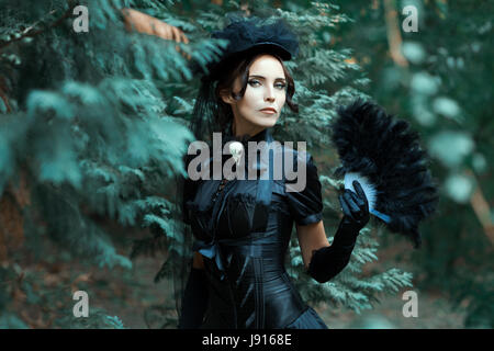 Mädchen in die gotische Statue Spaziergänge im Park. In ihren Händen hält sie ein Fan. Stockfoto