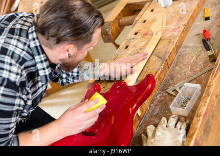 Nahaufnahme des Handwerkers Schleifen einen Gitarrenhals aus Holz in Werkstatt Stockfoto