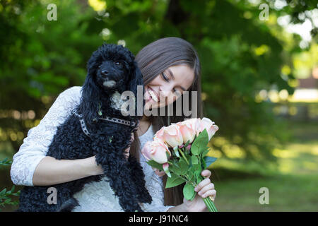 Junge Frau mit ihrem Hund im Park genießen. Überrascht die Blumen, die sie erhalten. Tiefenschärfe und kleine Schärfentiefe Stockfoto