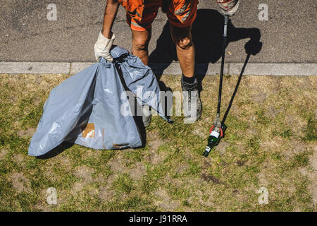 Person Reinigung Park mit einem Papierkorb Grabber - Stadt Service Arbeitnehmer Abholung Müll mit einem Greifer-Stock Stockfoto