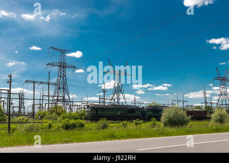 Güterzug verläuft durch thermische Kraftwerke und Stromleitungen. Verteilung elektrische Unterstation Stockfoto