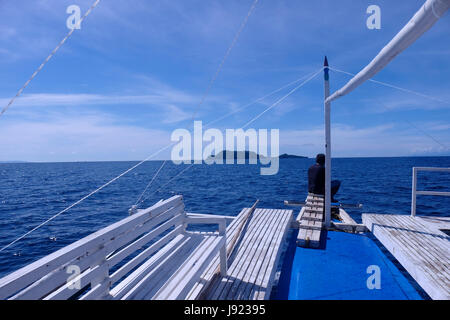 Ein Filipino Mann sitzt auf dem Deck eines Bootes Annäherung an der Westseite des Apo Island eine Insel vulkanischen Ursprungs aus der südöstlichen Spitze der Insel Negros in den Philippinen. Stockfoto