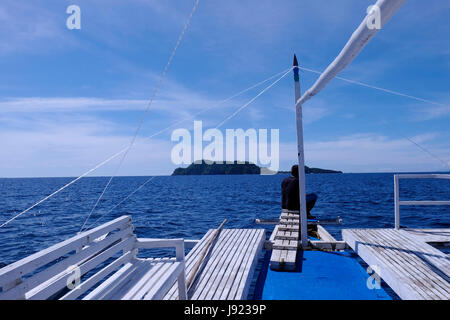 Ein Filipino Mann sitzt auf dem Deck eines Bootes Annäherung an der Westseite des Apo Island eine Insel vulkanischen Ursprungs aus der südöstlichen Spitze der Insel Negros in den Philippinen. Stockfoto