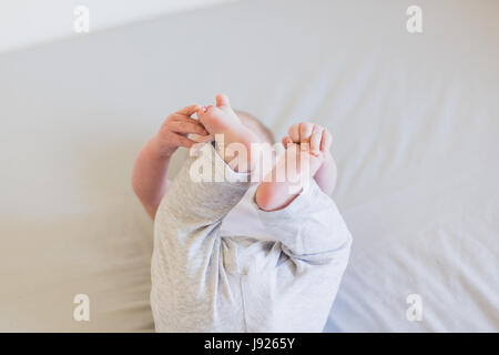 Vier Monate altes Baby junge neugierig mit seinen Zehen drinnen spielen Stockfoto