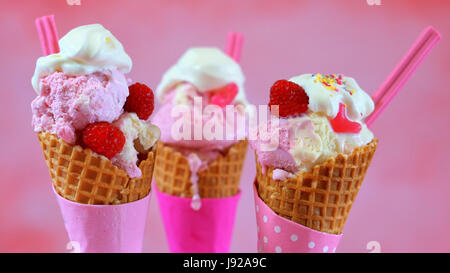 Sommer rosa Eistüten mit Süßigkeiten und Obst, Meling vor einem hellen rosa Hintergrund geschmückt. Stockfoto