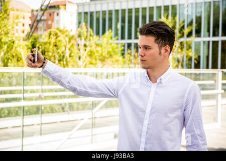 Junger Mann lächelnd und Aufnahme mit Handy Stockfoto