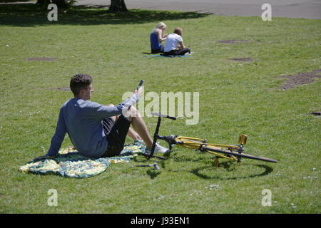 Glasgower heraus in die Grünflächen der Kelvingrove Park als die Temperaturen stiegen für den zweiten Tag in ein Zeile junge mit smart Handy-Mädchen Stockfoto