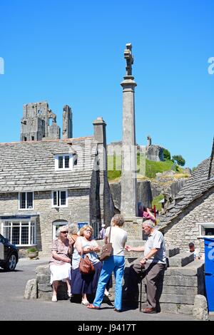 Touristen um den Stein herum kreuzen im Zentrum Dorfes mit dem Schloss auf der Rückseite, Corfe, Dorset, England, Vereinigtes Königreich, West-Europa. Stockfoto