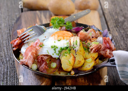 Bauernfrühstück mit Bratkartoffeln, Spiegelei und Speck in einer Eisenpfanne serviert Stockfoto