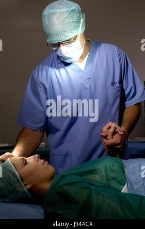 Chirurg im OP-Saal mit Mundschutz und OP-Cap bereitet Frau Patient weiblich Stockfoto