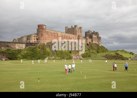 Cricket-Spiel vor Bamburgh Castle, Northumberland, England. Stockfoto