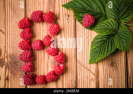 Buchstabe B von Himbeeren mit Blättern auf einer Holzfläche, Nahaufnahme Stockfoto