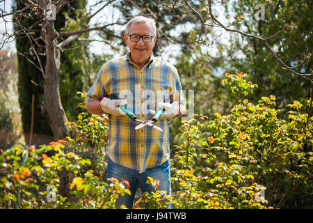 Ältere Mann in seinem Garten. Er wird um die Pflanzen zu trimmen. Stockfoto