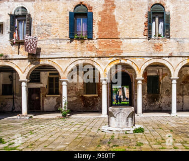 Kreuzgang der Basilika di San Pietro di Castello Innenhof mit Bögen & überdachten Gehweg, Brunnen, historische Kirchengebäude verwittert. Venedig, Italien Stockfoto