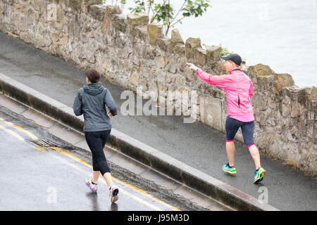 Zwei Frauen joggen mit einem Hinweis darauf, wie Sie entlang der Küstenstraße rund um die Great Orme in Llandudno an einem regnerischen Sommertag jog Stockfoto