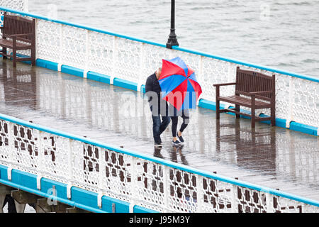 Ein paar Auseinandersetzung mit ihren bunten Regenschirm zum Schutz vor der nassen und windigen Wetter auf dem Holzsteg von Llandudno Pier in der touristischen Stadt von Llandudno, Nordwales Stockfoto