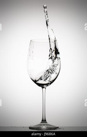 Wasser spritzt in ein Glas Wein auf einem Farbverlauf Hintergrund Stockfoto