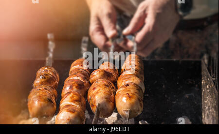 Leckere, saftige Würstchen am Spieß über offenem Feuer gegrillt. Die Hand, die die Spieße. Stockfoto