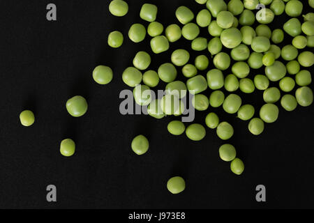 Grüne Erbsen verstreut, frisch gepflückt, auf schwarzem Hintergrund. Ansicht von oben Stockfoto