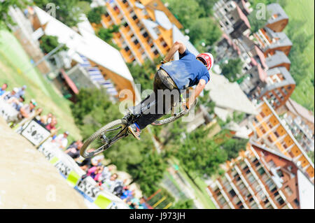 Mann springt mit seinem MTB während einer Freeride World Tour-Meisterschaft in Frankreich vor Zuschauern (hier im Dorf von "Deux Alpes") Stockfoto