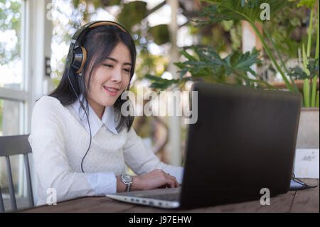 Junge attraktive Asiatin Musik hören während der Arbeit online mit Laptop im Café. Freier Mitarbeiter und selbständige Business act Stockfoto