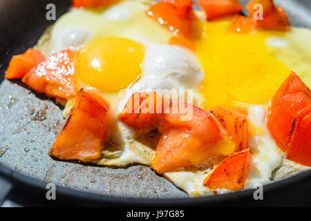 Rührei mit Tomaten in einer Pfanne erhitzen. Der Prozess der Zubereitung des Frühstücks Stockfoto