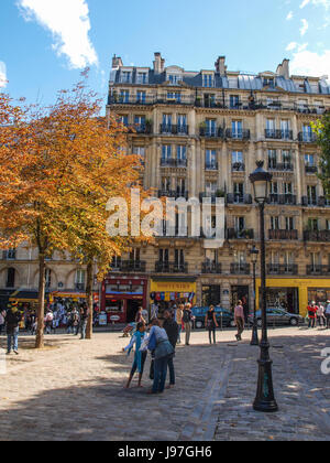 Paris-Straßenszene im Herbst mit Orangenbaum. Region des Montmartre in Paris, Frankreich. Gepflasterte Straße ist gesäumt von Bäumen und Laternenmasten. Stockfoto