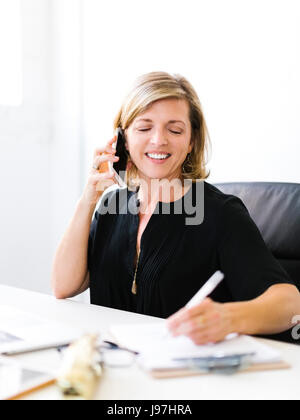 Reife Frau am Handy und Notizen Stockfoto