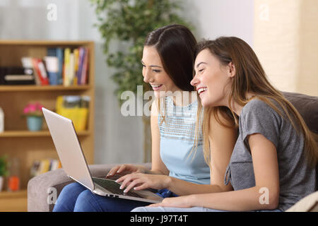 Zwei glückliche Freunde Lachen beobachten Medieninhalte in einem Laptop auf Linie sitzen auf einer Couch im Wohnzimmer zu Hause Stockfoto