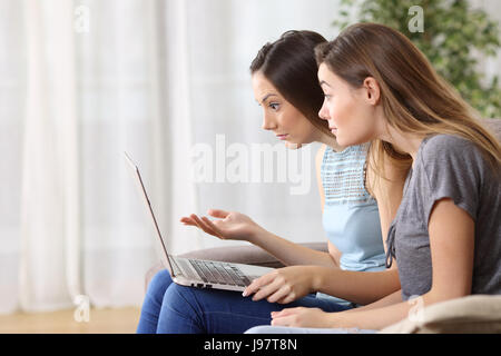 Seitenansicht der beiden verärgert Mitbewohner beobachten Medieninhalte in einem Laptop auf Linie sitzen auf einer Couch im Wohnzimmer zu Hause Stockfoto
