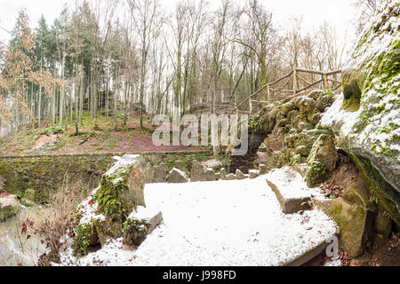 tief im Wald gibt es einen kleinen Wasserfall in der Schweiz in Luxemburg mit Schnee Stockfoto