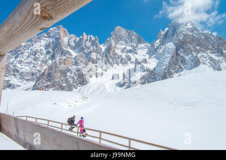 Zwei Wanderer Freunde betrachten die schönen Berge vor ihnen sitzen auf einem hölzernen Zaun und Einweichen in der Sonne, auf dem Schnee reflektiert. Stockfoto