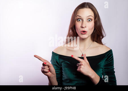 Portrait von überrascht, schockiert Frau mit Sommersprossen und klassischen grünen Kleid leeren Raum mit Finger zeigen. Studio auf Silber grauen Hintergrund gedreht. Stockfoto