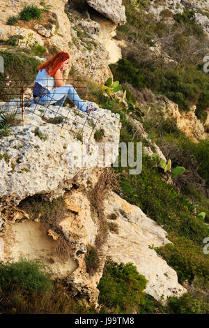 Eine Flamme dunkelhaarige Mädchen sitzt auf einer Klippe in Dingli Cliffs, Malta Stockfoto