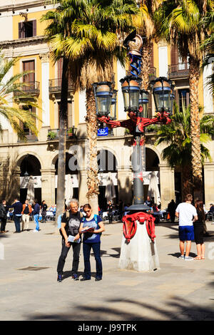 Touristen unter einem Gaudis Straßenlaternen in Placa Reial im Bereich Barri Gotic in Barcelona, Katalonien, Spanien. Stockfoto