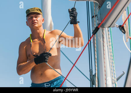 Schöner junger Mann verwaltet ein Segelboot. Anpassung der Ausrüstung. Luxus-Sport und Erholung. Stockfoto