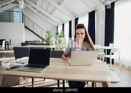Foto von junge fröhliche Dame sitzt im Büro coworking mit Laptop Computer Chat per Telefon. Blick in die Kamera. Stockfoto